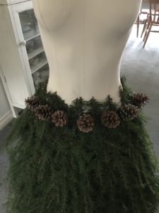 Fir tree branches and pine cones create mannequin skirt for christmas decor