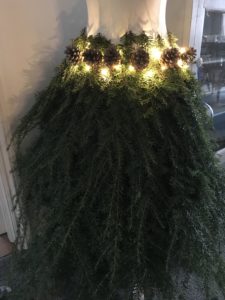 Fir tree branches pine cones and battery fairy lights create mannequin skirt for christmas decor