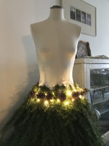 Fir tree branches pine cones and battery fairy lights create mannequin skirt for christmas decor