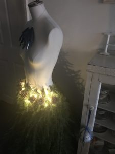 Fir tree branches pine cones and battery fairy lights and baubles create mannequin outfit for christmas decor