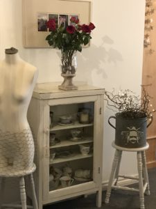 mannequin and zinc planter on painted bar stools with vintage china cabinet and red roses in hurricane lamp