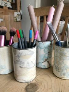 four tin cans covered in blue wallpaper with assortment of brushes candles and coloured felt pens