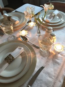 distressed plate charger with white plates, napkin and gold napkin ring, candles and wine glasses