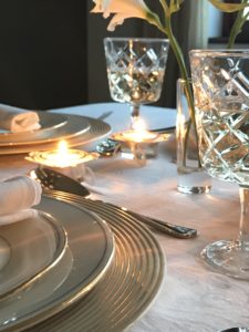 distressed plate charger with white plates, napkin and gold napkin ring, candles and wine glasses