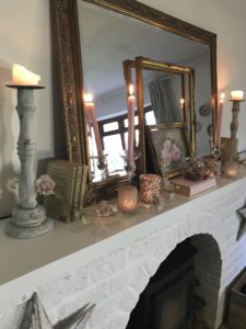 white painted fireplace with brass mirror frames books pictures candlesticks and rose garland