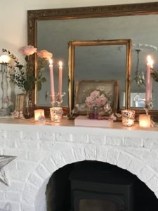 white painted fireplace with brass mirror frames books pictures candlesticks pink roses and rose garland