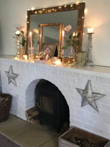 pink roses candles vintage french books rose garland and gilt mirror and frames on white painted fireplace with woodburer and fairy lights