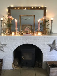 pink roses candles vintage french books rose garland and gilt mirror and frames on white painted fireplace with woodburer and fairy lights