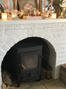 white painted fireplace with woodburner and pink decoration including book candles and foliage