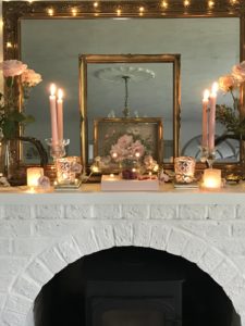 white painted fireplace with pink decoration including book candles gilt mirror and frames