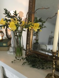 daffodils, books, foliage mirror and candlestick on white painted fireplace