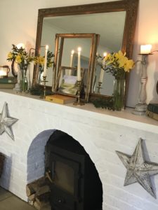 distressed star on white painted fireplace with mirror frames daffodils wreath books candles stars and wood burner