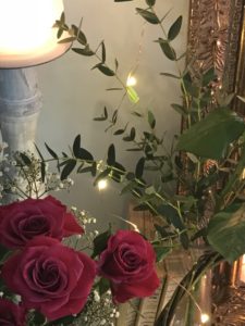 dark pink roses green foliage twinkle lights and candlestick and gilt frame on painted fireplace