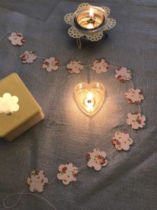 card flower paper garland with hole punch and tealight on blue table runner