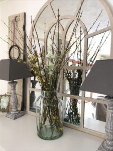 green glass jar with stems, lamps, shutters and mirror on painted sideboard