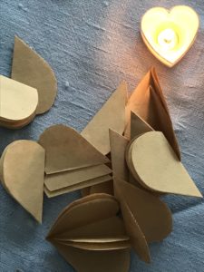 heart shape cuts from brown paper with tealight on blue table runner