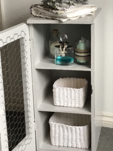 dried blue hydrangea white towel and glass bottles and rattan storage inside grey painted pot cupboard