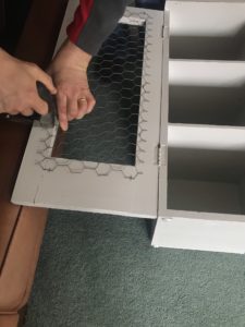 hands attaching chicken wire to inside door of painted pot cupboard with stapler