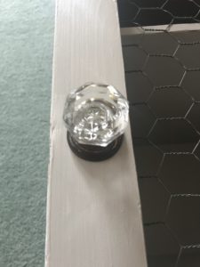 vintage glass door knob on door of grey painted pot cupboard and chicken wire