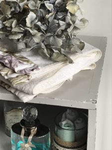 dried blue hydrangea white towel and glass bottles inside grey painted pot cupboard