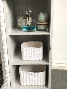 pretty glass bottles and white rattan storage baskets on shelves inside grey painted pot cupboard