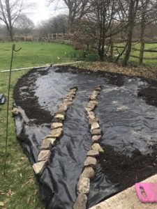 preparing path of rocks on weed suppresent before topsoil for wildflower garden