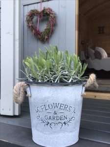 lavender in pot on steps of shepherds hut with grass wreath heart in wildflower garden