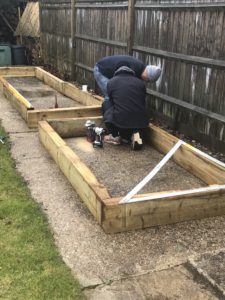 men creating raised beds on concrete base by fence pannels in vegetable garden