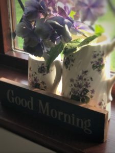 two lilac flowered jugs with hydrangea and good morning sign