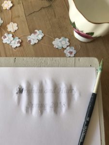 transferring word letters to vintage garden tray with paper flower garland and jug and brush