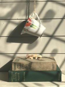 orange gerbera milk jug hanging on string above vintage books, heart garland and filtered light