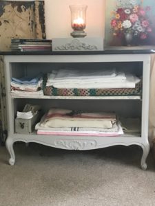 painted linen storage cabinet with linens, candles, books and painting