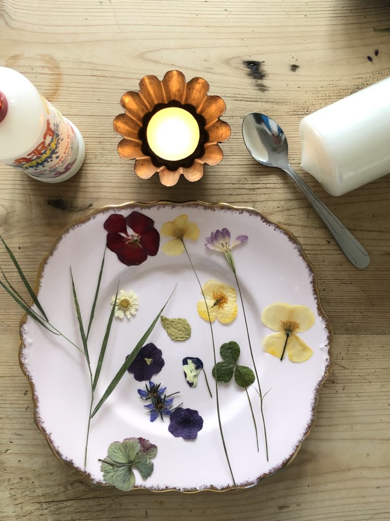 flatlay of pink plate with dried flowers, candle, teaspoon and craft glue to make pressed flower candles