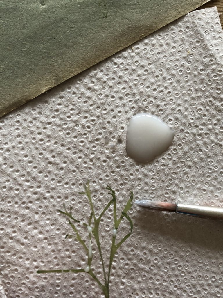 blob of craft glue on white paper towel with paint brush and grass head for making pressed flower candles