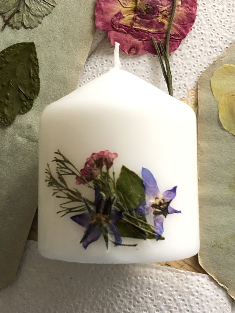 white stubby candle with variety of pressed flowers pressed into candle