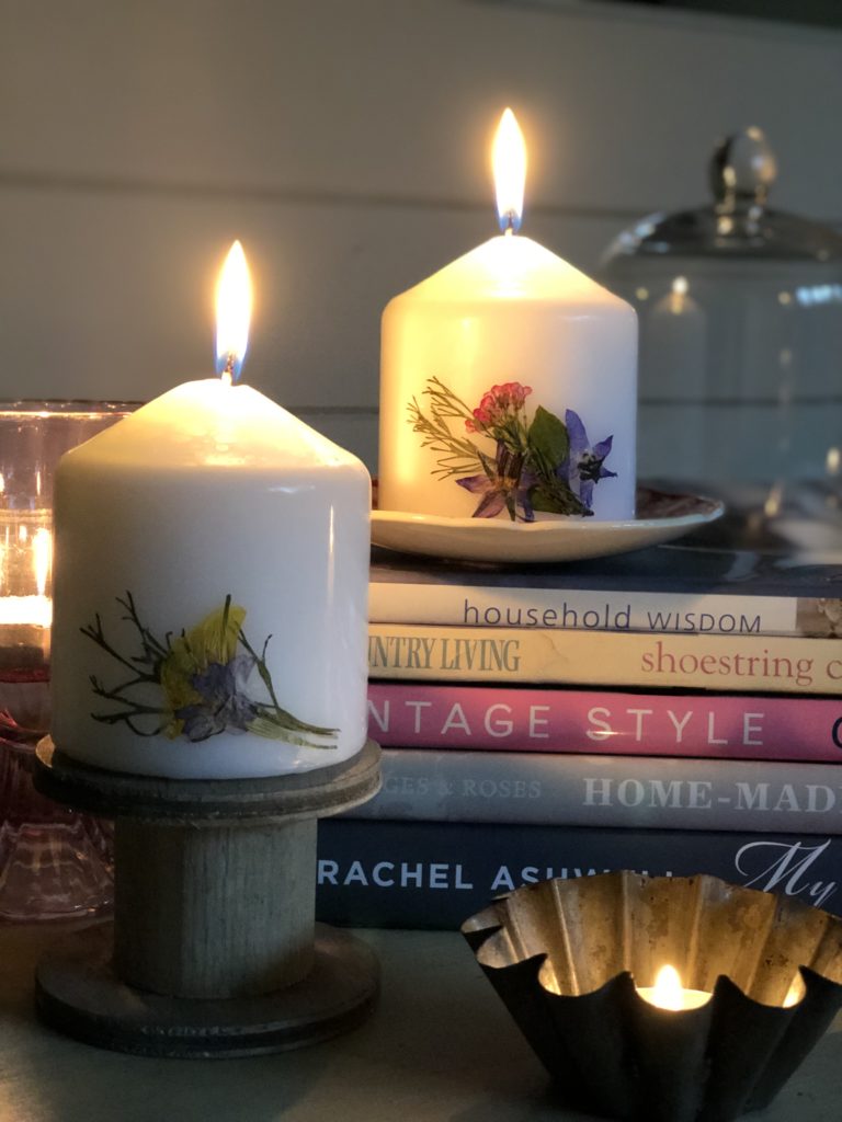 two pressed flower candles glowing on book stack with spool