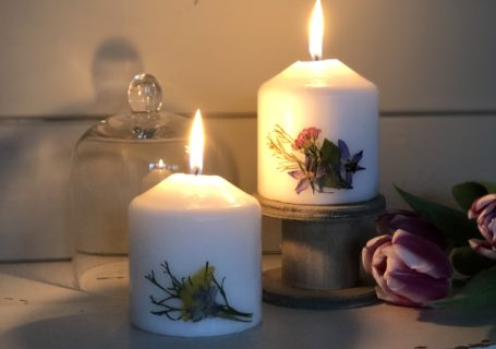 two pressed flower candles glowing on chippy white table with tulips and cloche