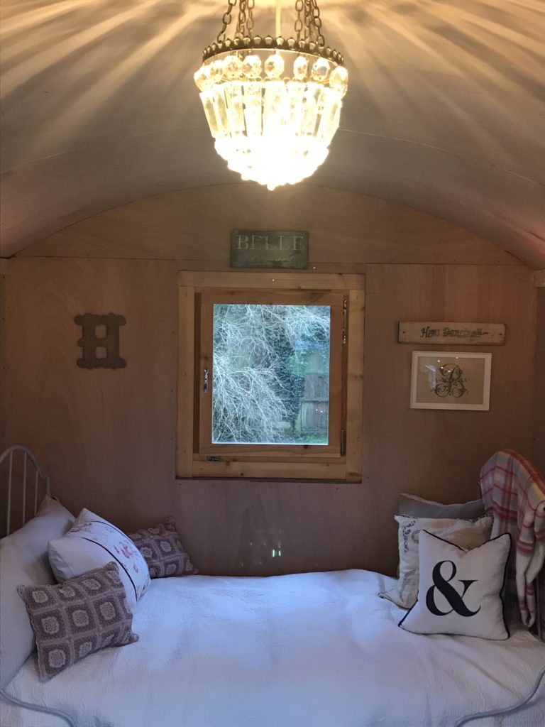 vintage chandelier wrought iron bed covered in bedspread and cushions inside shepherds hut