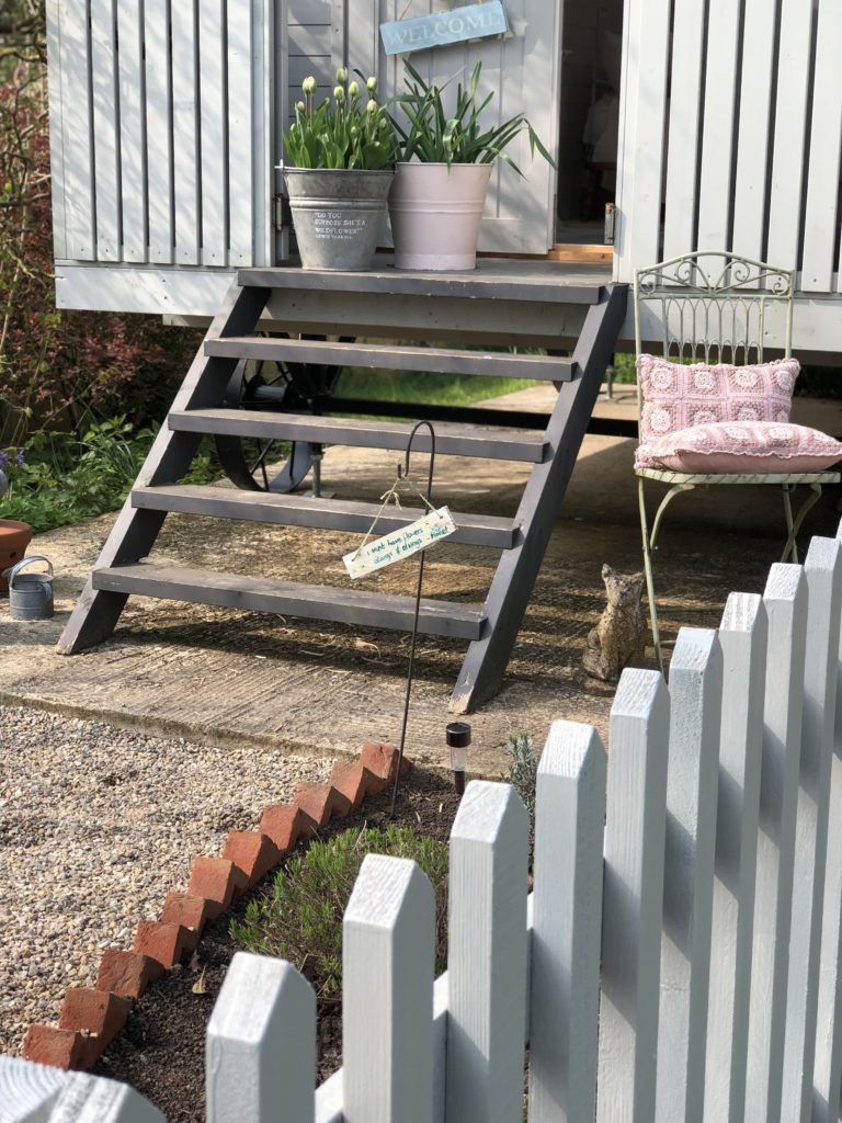 wooden steps gravel path picket fence and iron chair with pink cushions in cottage garden