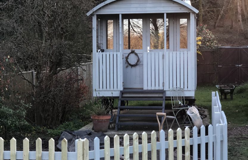 white picket fence surrounding potential small cottage garden in front of painted shepherds hut