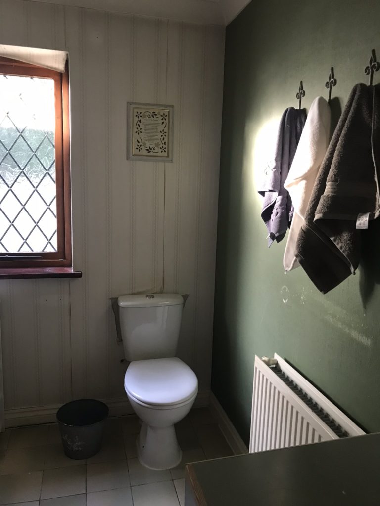 tatty  bathroom with white toilet, towels and peeling wallpaper