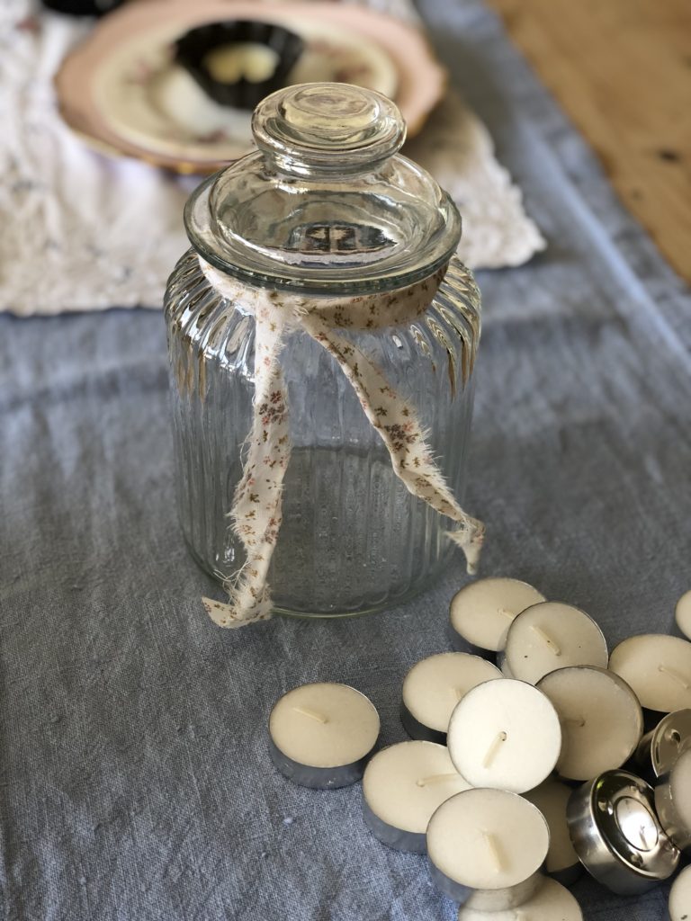 empty glass bon bon jar with ribbon and tealights on table top