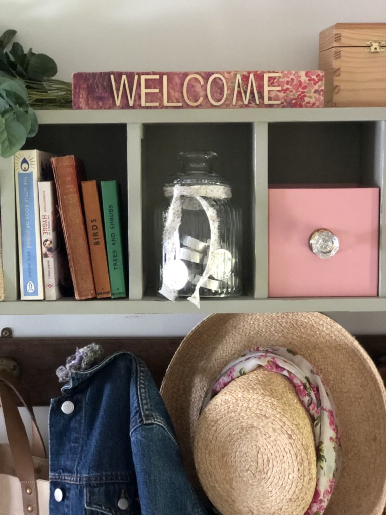 recycled cd storage unit with glass jar, books, pink box an hats and jackets