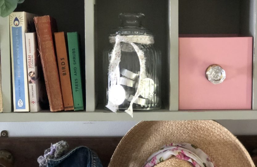 recycled cd storage unit with glass jar, books, pink box an hats and jackets