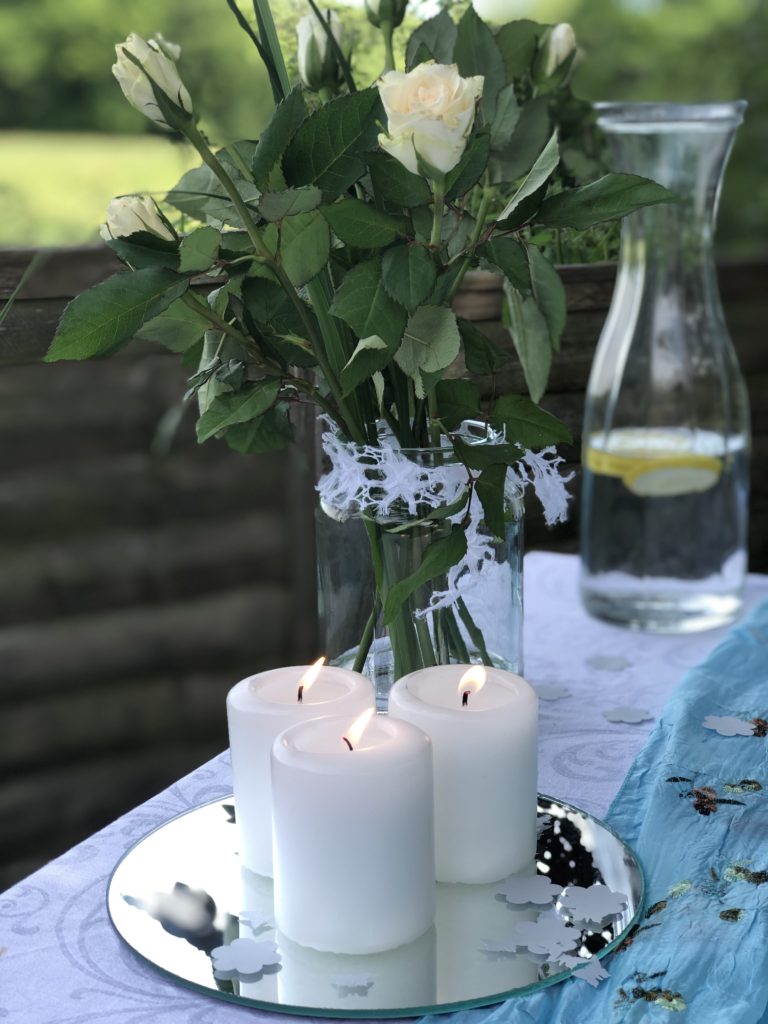 three white pillar candles and paper confetti on top of mirror with white roses