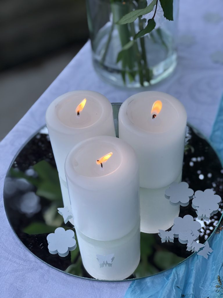 three white pillar candles and paper confetti on top of mirror