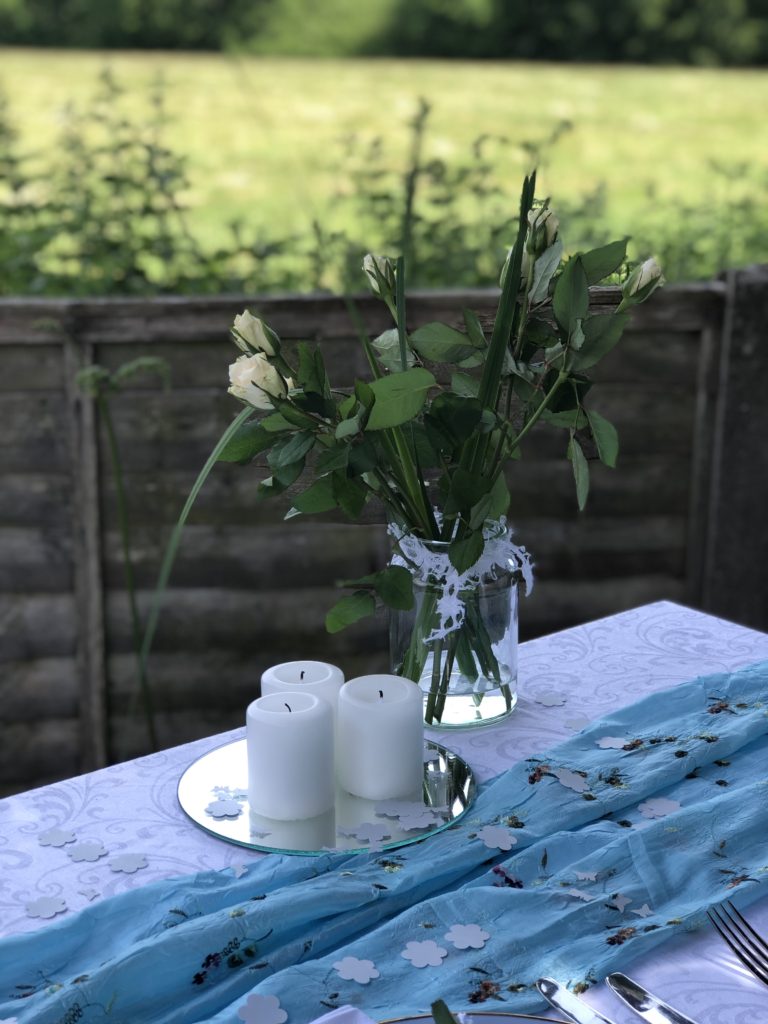 three white pillar candles and paper confetti on top of mirror with white roses