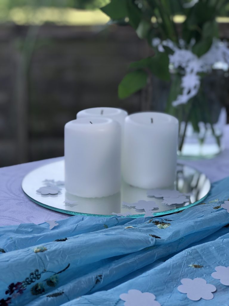 three white pillar candles and paper confetti on top of mirror