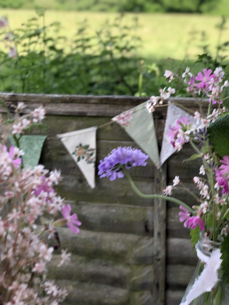 homemade bunting on fence with homegrown flowers