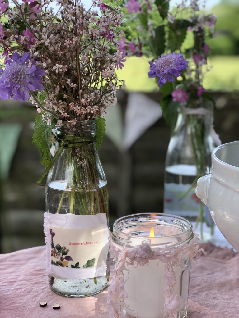 homegrown flowers in recycled bottle with candles create simple table decoration for summer dining